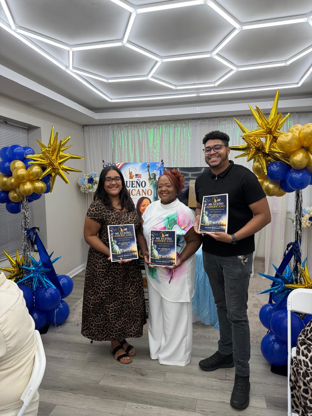 Tres asistentes mostrando sus libros frente a los arreglos azules y dorados.